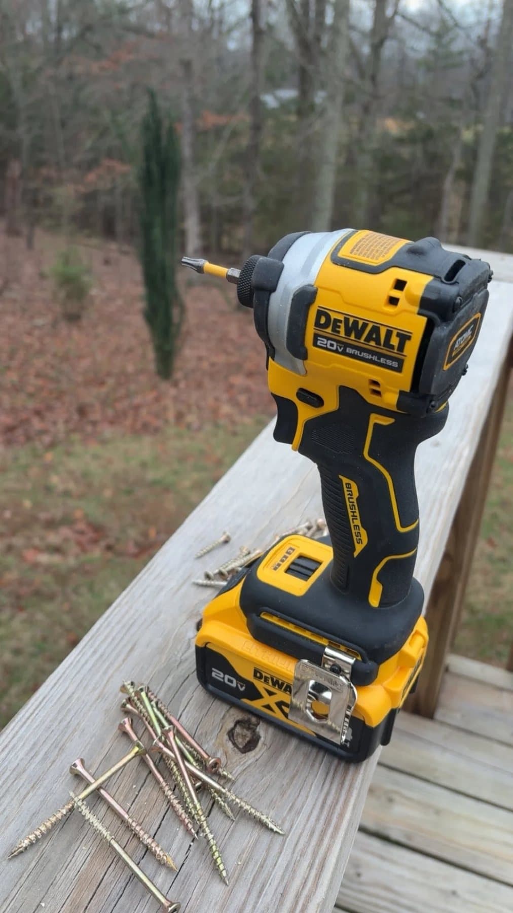 DeWalt impact driver on a deck railing with a pile of screws